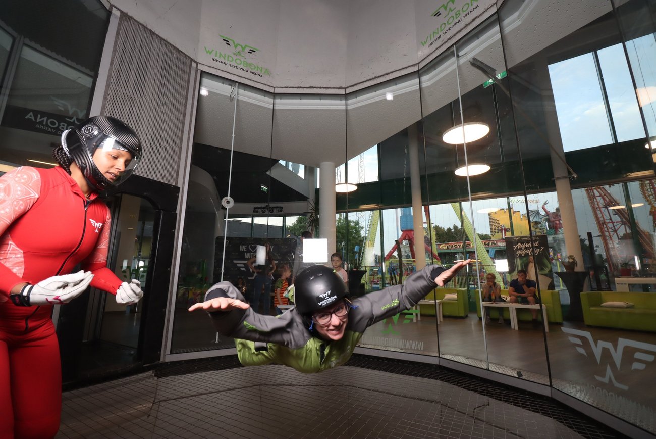 Zwei Personen in einem Windkanal, eine steht, eine fliegt.