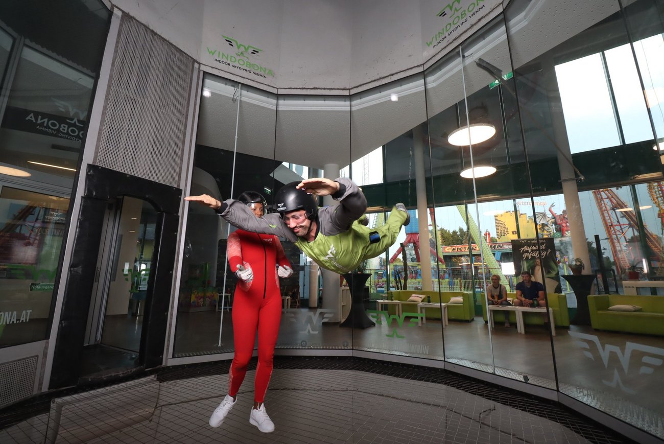 Zwei Personen in einem Windkanal, eine steht, eine fliegt.