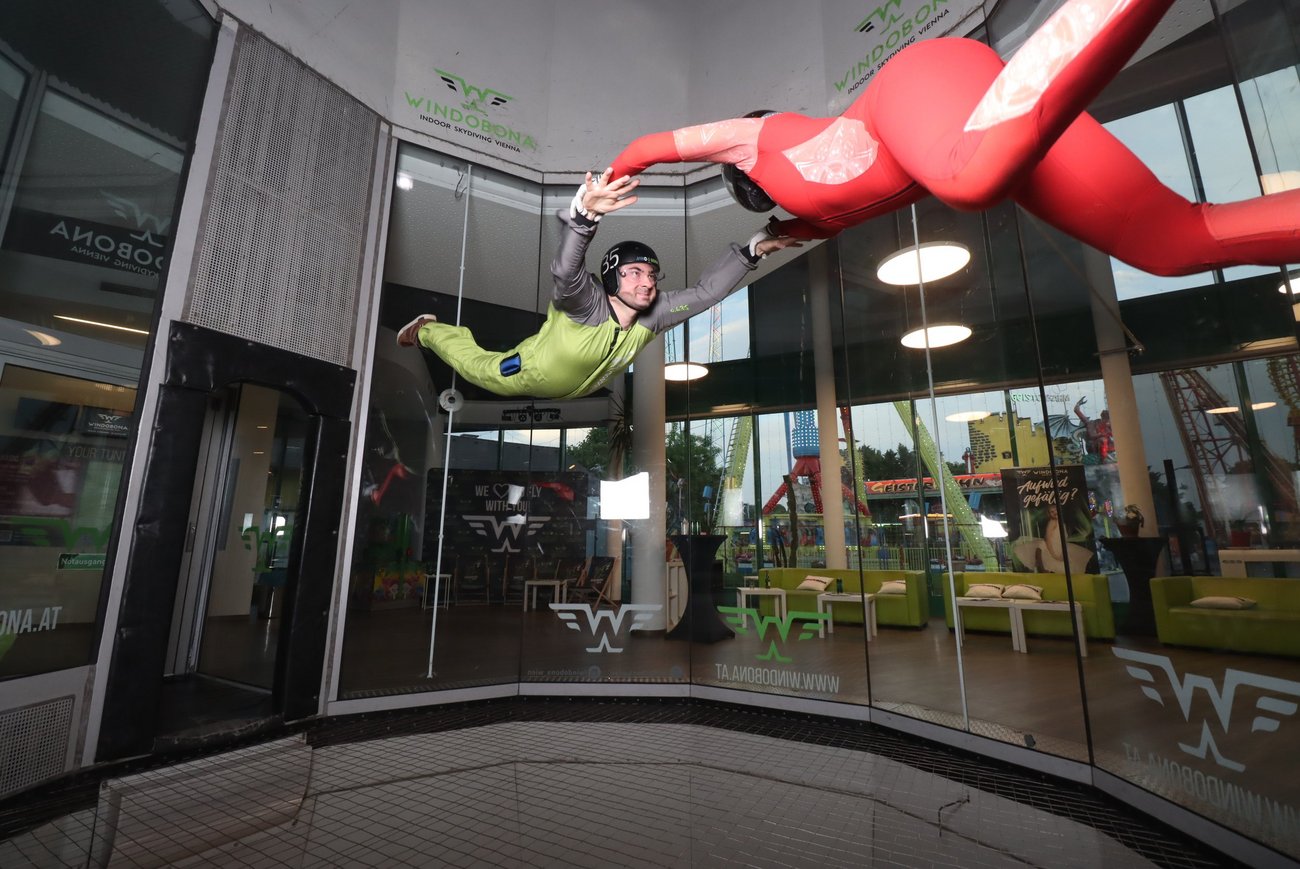 Zwei Personen in einem Windkanal, eine steht, eine fliegt.